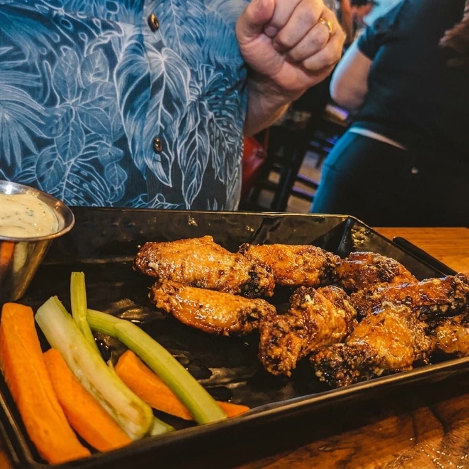 Crispy chicken wings with carrots, celery, and ranch dip on a black plate at a bar.