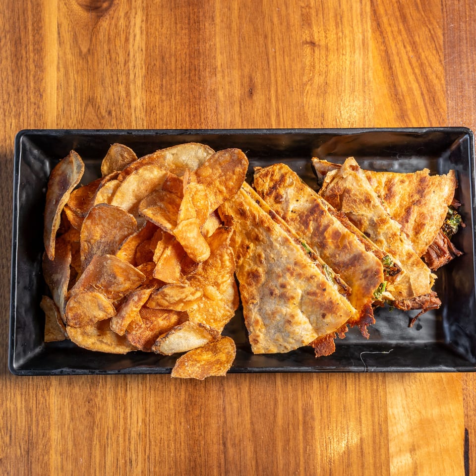 Black platter holding crispy potato chips and golden fried stuffed pastries on a wooden table.