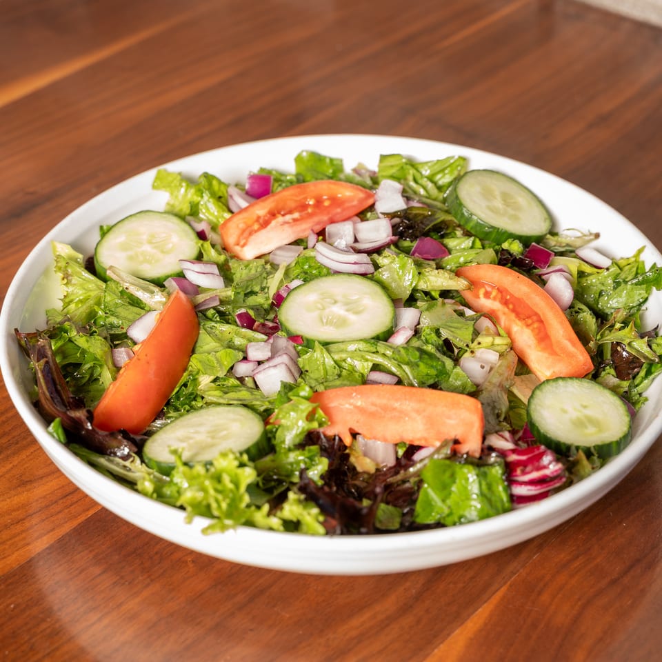 Fresh green salad with lettuce, sliced cucumbers, tomatoes, and red onions in a white bowl on a wooden table.
