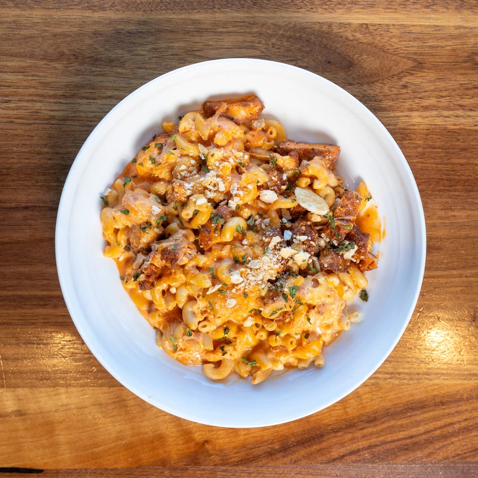 Overhead view of creamy orange macaroni pasta topped with crispy meat, breadcrumbs, and chopped herbs on a white plate.