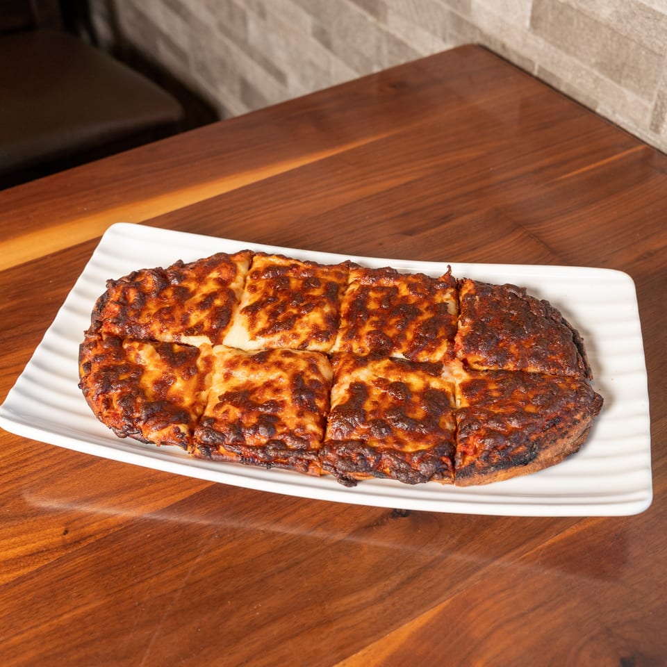Golden-brown, cheese-topped baked dish cut into squares on a white platter atop a wooden restaurant table.